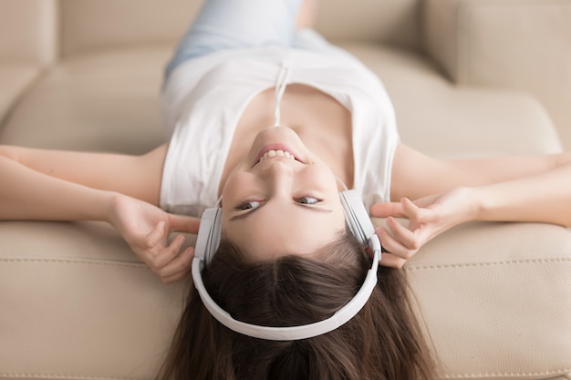 Mujer joven que miente en el sofá con los auriculares en la cabeza