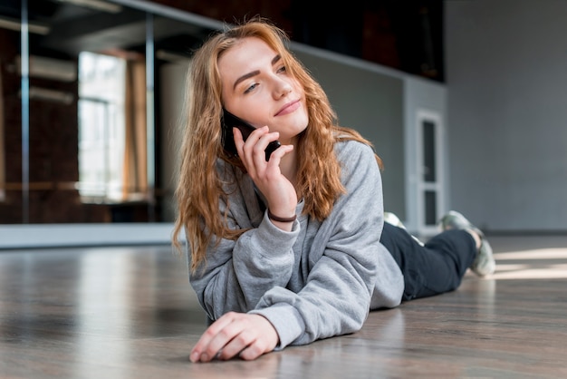 Foto gratuita mujer joven que miente en el suelo de madera dura que habla en el teléfono móvil