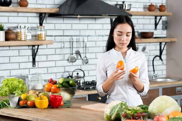 Mujer joven que mira dos medias naranjas en cocina en casa