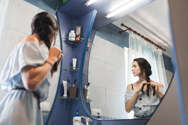 Mujer joven que mira en el espejo que ata su pelo