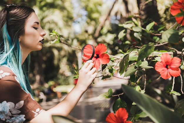Mujer joven que mira la flor del hibisco a través de la lupa