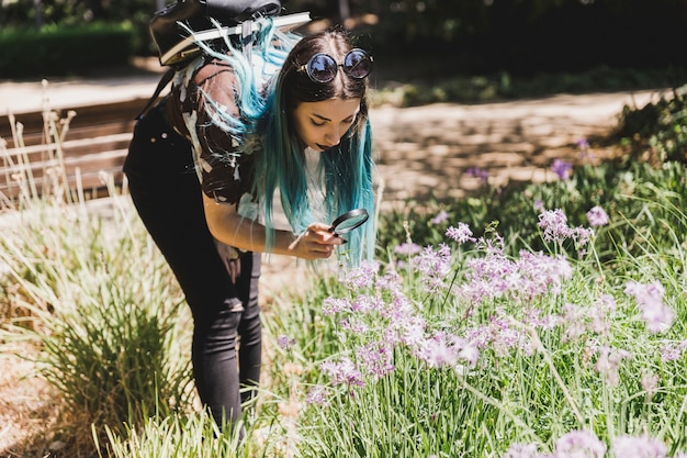 Mujer joven que mira las flores salvajes a través de la lupa