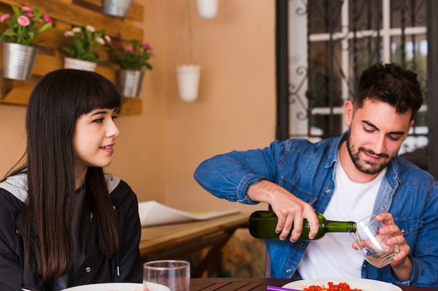 Mujer joven que mira el hombre que vierte el alcohol en vidrio