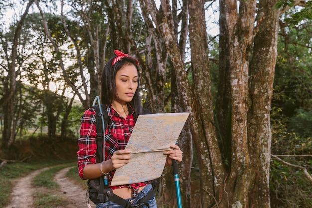 Mujer joven que mira el mapa mientras que camina en bosque