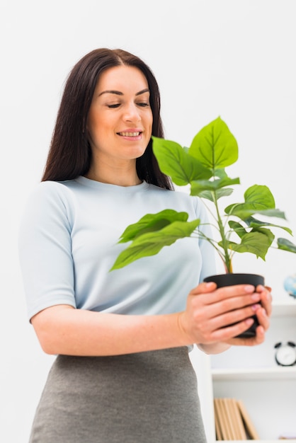 Foto gratuita mujer joven que mira la planta verde en maceta