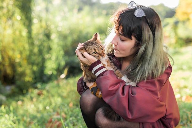 Foto gratuita mujer joven que mira su gato de gato atigrado en parque
