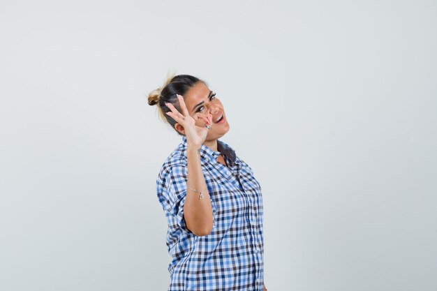 Mujer joven que muestra un gesto aceptable en camisa a cuadros y parece satisfecho.