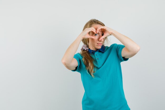 Mujer joven que muestra el gesto del corazón en camiseta y parece optimista.