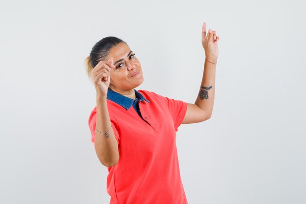 Mujer joven que muestra el gesto de la danza en la camiseta roja y que parece bonita. vista frontal.