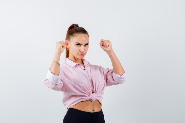 Mujer joven que muestra el gesto del ganador en camisa casual, pantalones y con suerte