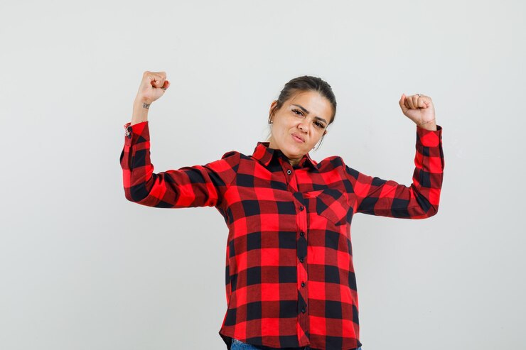 Foto gratuito mujer joven que muestra el gesto del ganador en camisa a cuadros y parece afortunado. vista frontal.