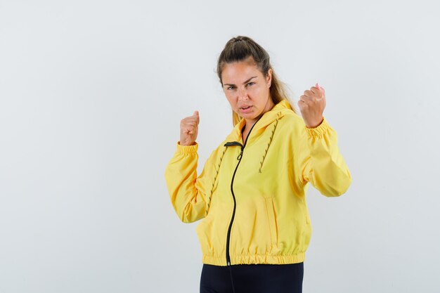 Mujer joven que muestra el gesto del ganador en chaqueta de bombardero amarilla y pantalón negro y parece seguro