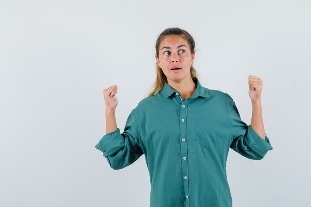 Mujer joven que muestra el gesto del ganador mientras mira a un lado con la camisa azul y parece afortunado