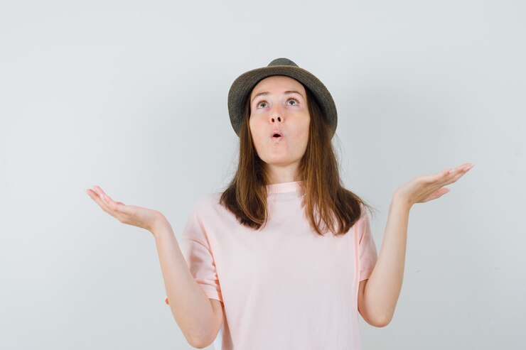 Foto gratuito mujer joven que muestra un gesto de impotencia en camiseta rosa, sombrero y mirada perpleja. vista frontal.