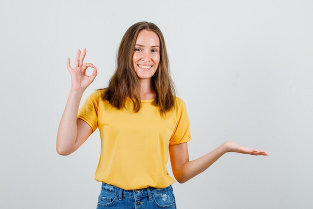 Mujer joven que muestra un gesto de ok con la palma abierta en camiseta, pantalones cortos y mirando alegre