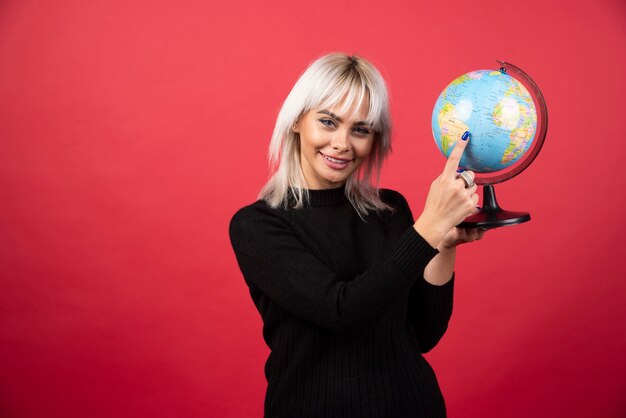 Mujer joven que muestra un globo terráqueo sobre un fondo rojo. Foto de alta calidad