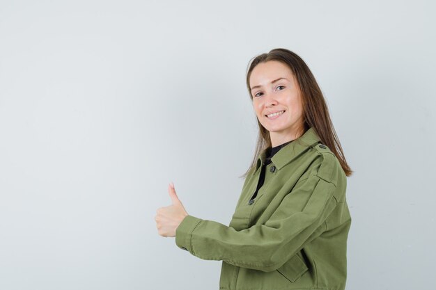 Mujer joven que muestra el pulgar hacia arriba en la chaqueta verde y parece positivo. .