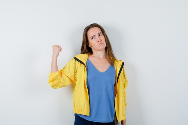 Mujer joven que muestra el puño cerrado en camiseta, chaqueta y parece seguro. vista frontal.