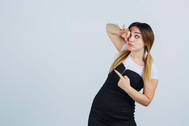 Mujer joven que muestra el signo de ok en el ojo mientras apunta a la izquierda