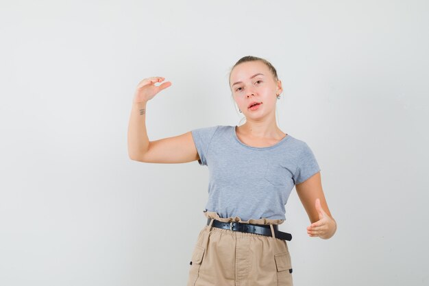 Foto gratuita mujer joven que muestra el signo de tamaño en la camiseta, vista frontal de los pantalones.