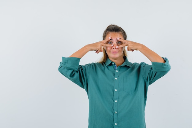 Foto gratuita mujer joven que muestra el signo v inverso en sus ojos en la vista frontal de la camisa azul.