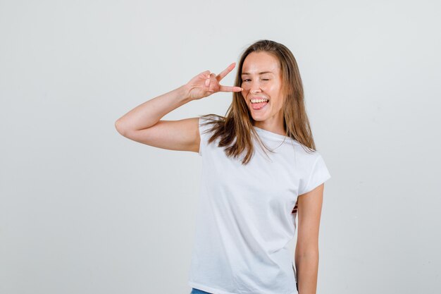 Mujer joven que muestra el signo v con parpadeo en camiseta, pantalones cortos y aspecto enérgico. vista frontal.