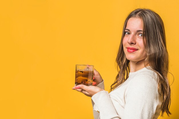 Mujer joven que se opone al fondo amarillo que sostiene la taza de infusión de hierbas