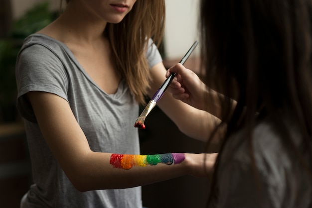 Mujer joven que pinta la bandera del arco iris sobre la mano de su novia con pincel