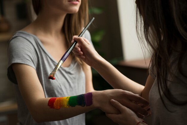 Mujer joven que pinta la bandera del arco iris sobre la mano de su novia