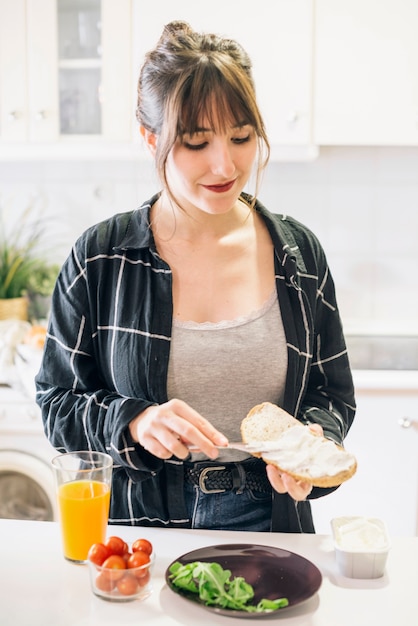 Mujer joven que pone queso en el pan en cocina