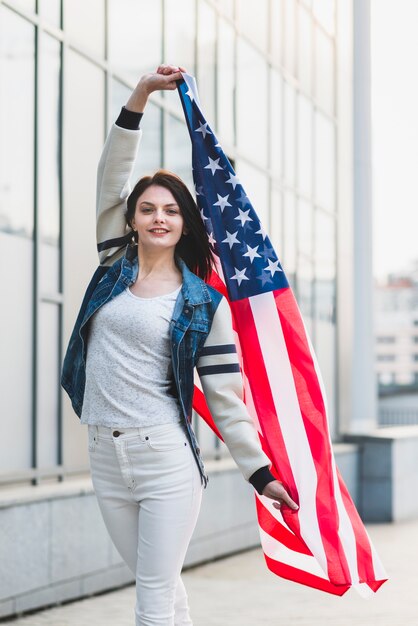 Mujer joven que presenta con la bandera americana de gran tamaño