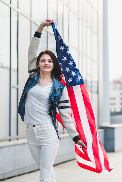 Mujer joven que presenta con la bandera americana de gran tamaño