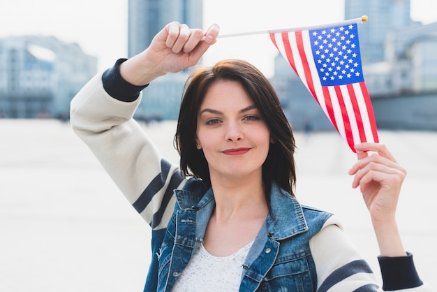 Mujer joven que presenta con la bandera de los EEUU sobre la cabeza