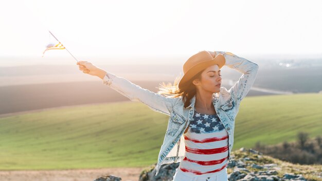 Mujer joven que presenta en camiseta de la bandera americana encima de la montaña