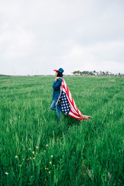 Mujer joven que se queda en el campo con la bandera americana