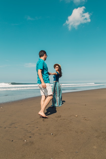 Mujer joven que quiere que su hombre siga a la línea de costa en la playa