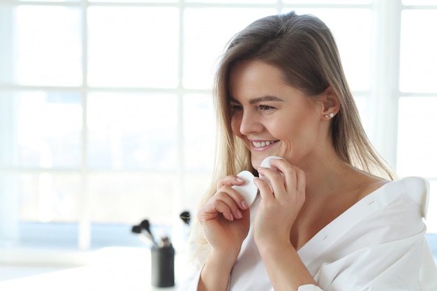 Mujer joven que quita maquillaje facial con toallitas desmaquillantes.