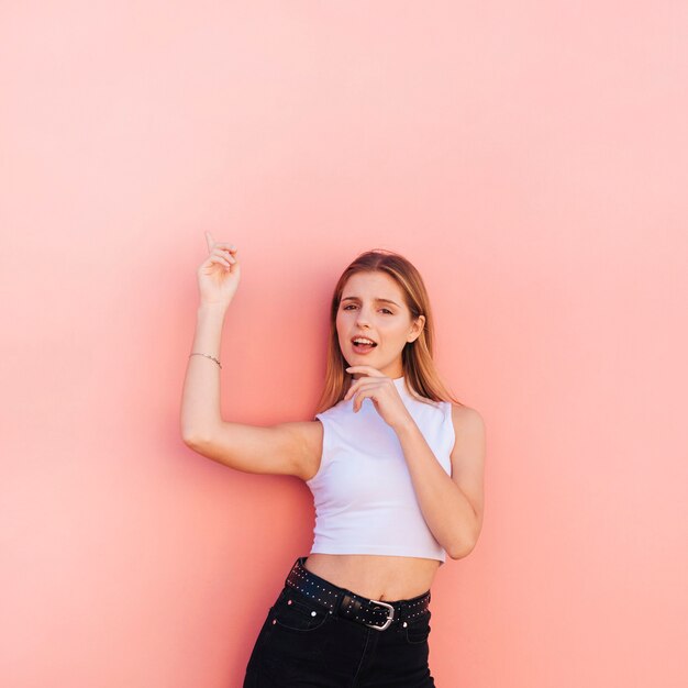 Mujer joven que señala los dedos hacia arriba contra el contexto coloreado