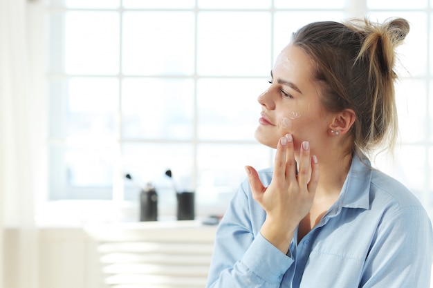 Mujer joven que se separa la crema facial. Concepto de cuidado de la piel.