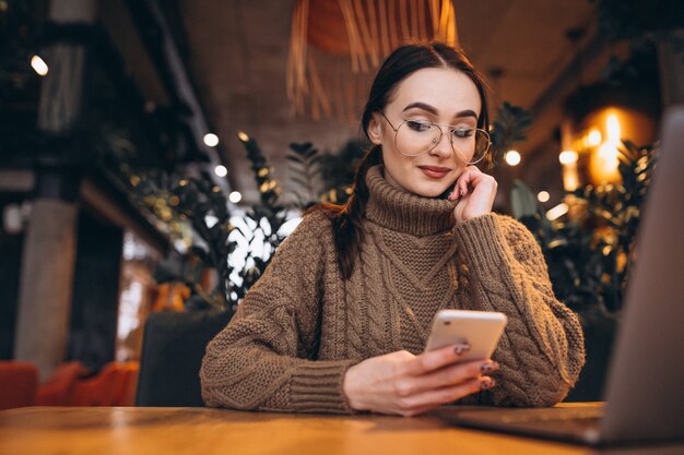 Mujer joven que se sienta en café y que trabaja en la computadora portátil