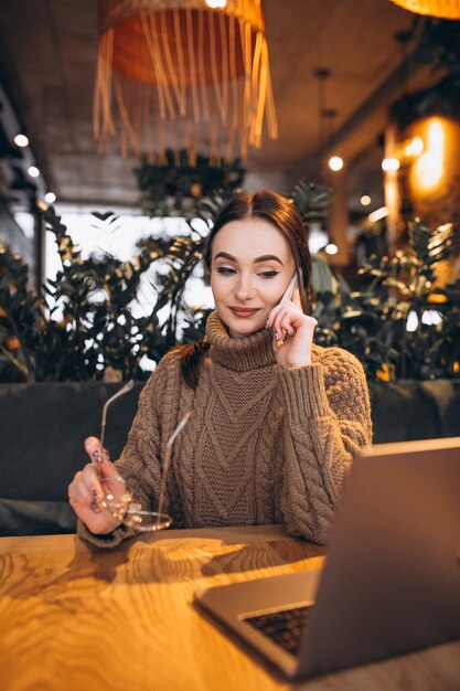 Mujer joven que se sienta en café y que trabaja en la computadora portátil