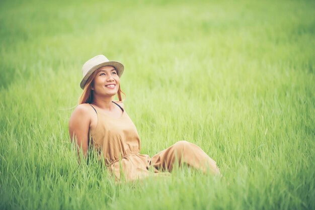 La mujer joven que se sienta se siente bien en campo de hierba.