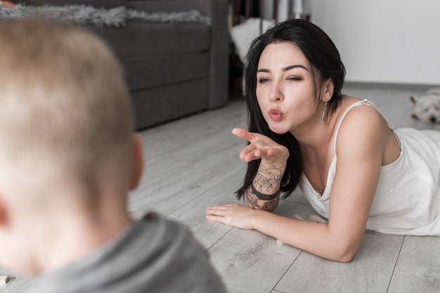 Mujer joven que sopla un beso a su hijo en la sala de estar