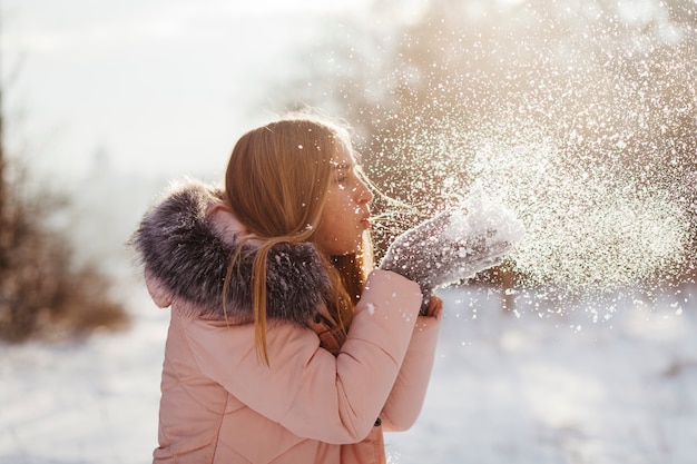 Mujer joven que sopla nieve de las manos