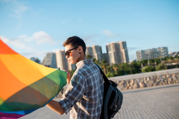 Mujer joven que sostiene la bandera de LGBT en la calle