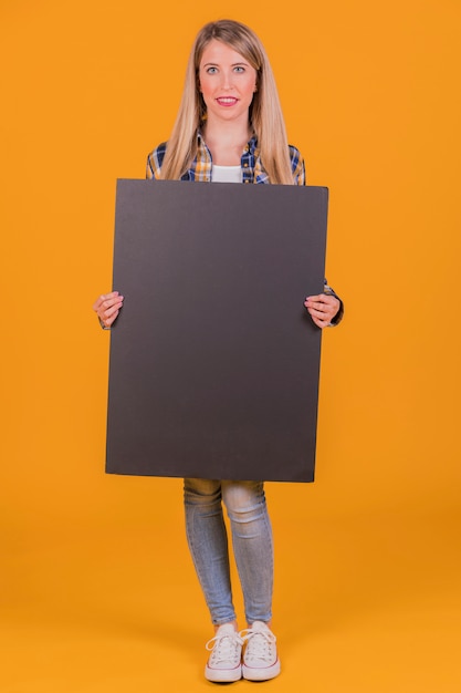 Una mujer joven que sostiene el cartel negro en blanco en la mano contra un fondo naranja