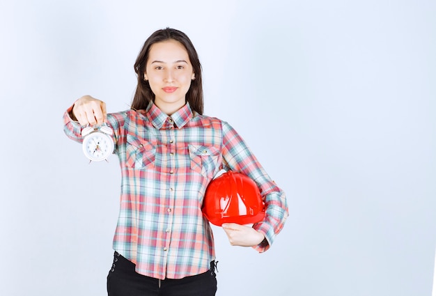 Una mujer joven que sostiene un casco y un reloj de alarma.