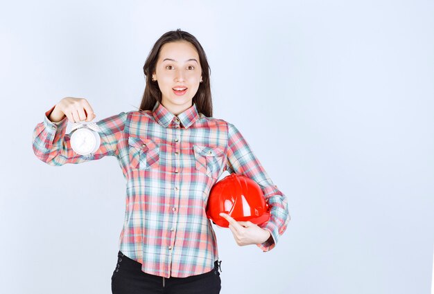 Una mujer joven que sostiene un casco y un reloj de alarma.