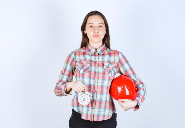 Una mujer joven que sostiene un casco y un reloj de alarma.