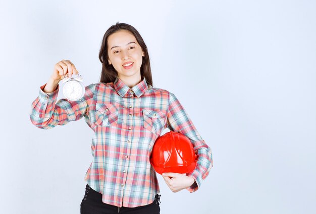 Una mujer joven que sostiene un casco y un reloj de alarma.